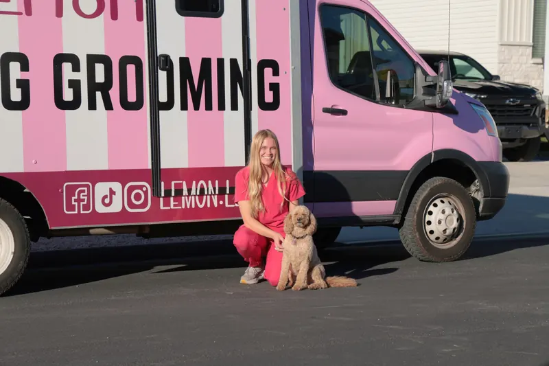 Camrie kneeling with a curly apricot dog beside the pink truck cab