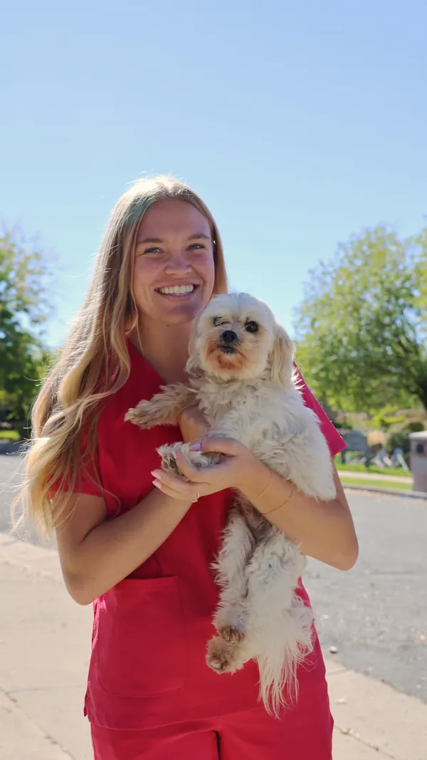 Camrie smiling and holding a small fluffy white dog outdoors